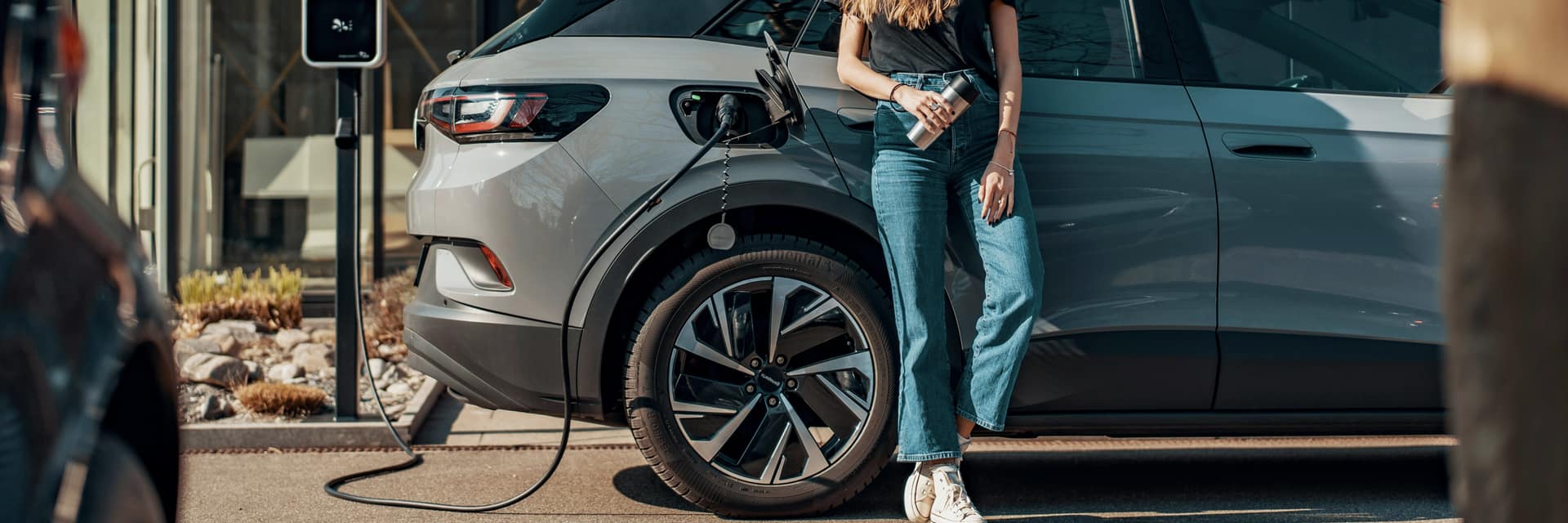 A woman standing next to an electric car while it charges