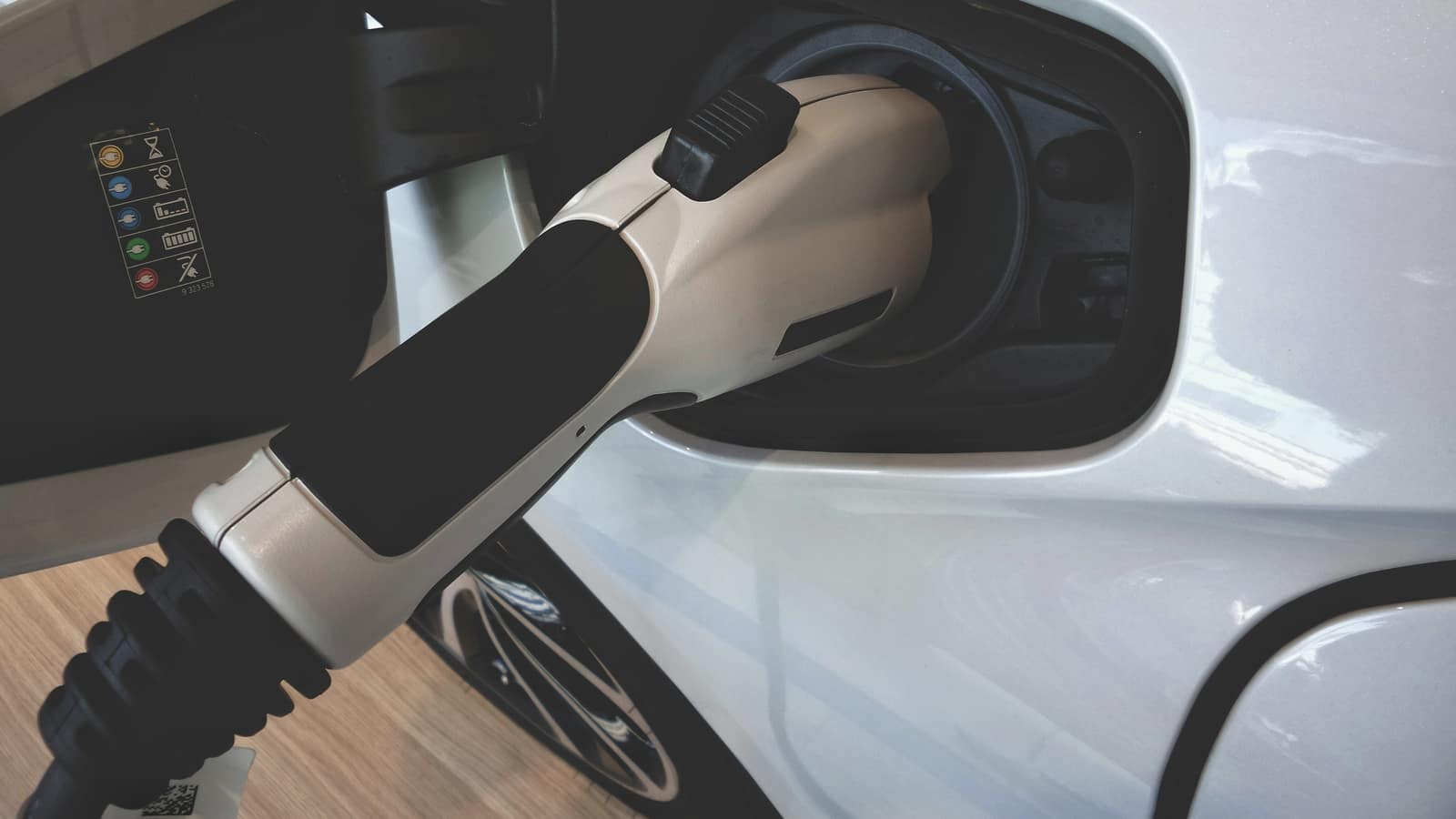 A charging connector plugged into the socket of a white electric car