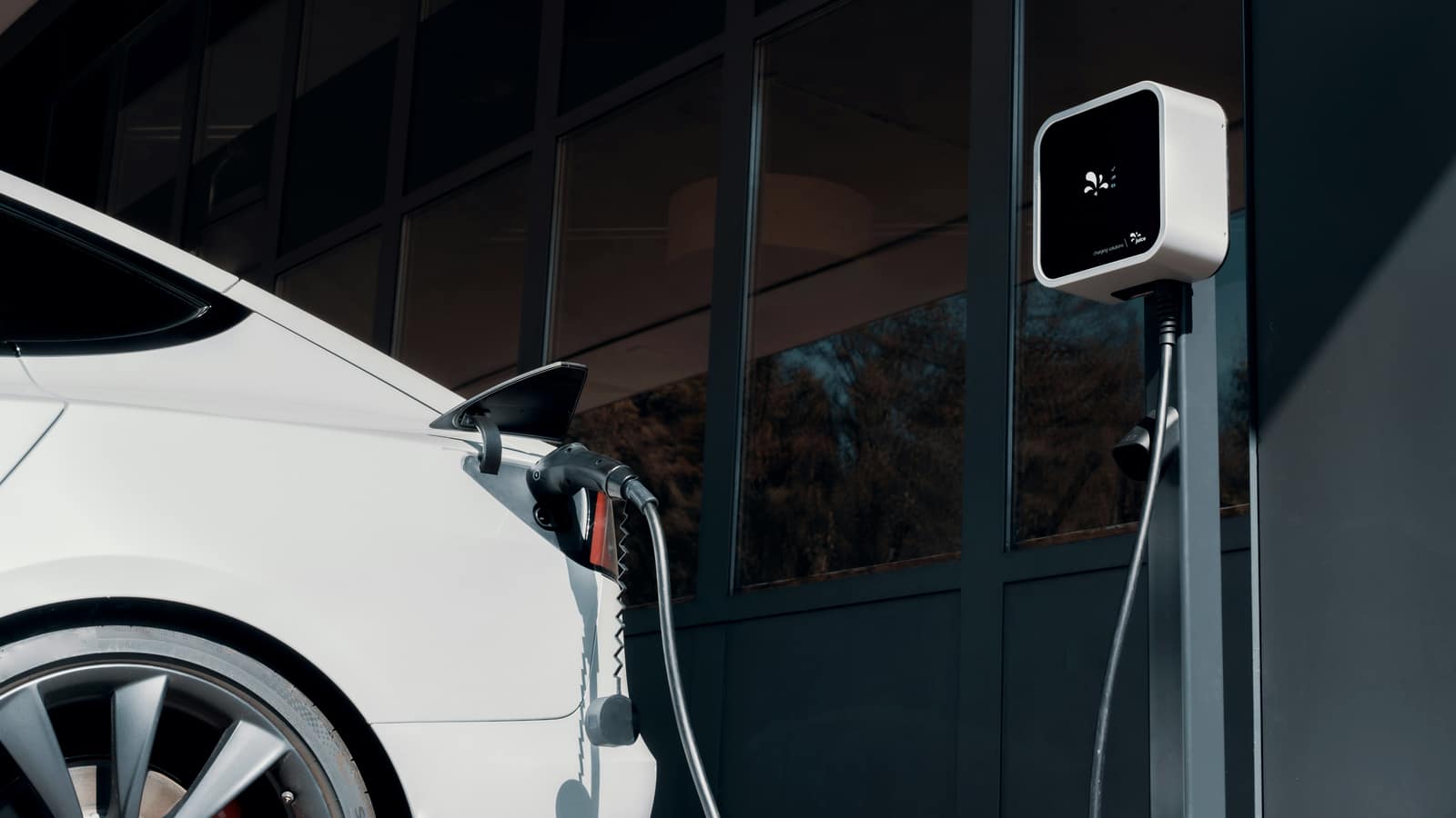 An electric car charging in front of a modern glass building
