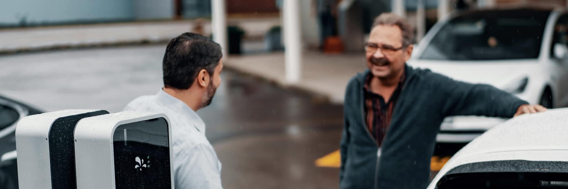 Two colleagues talking beside an electric car plugged into a charging point