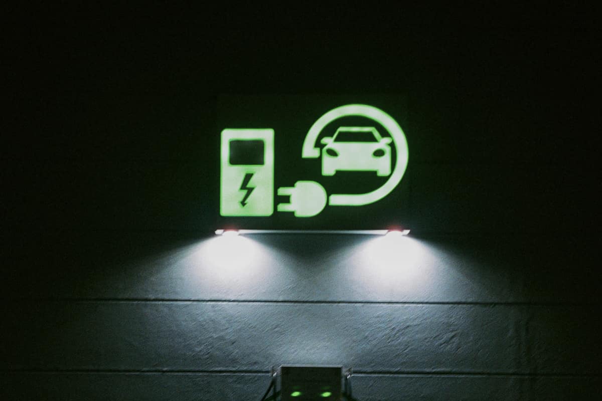 A glowing neon sign of a charging plug above an EV charging point at night
