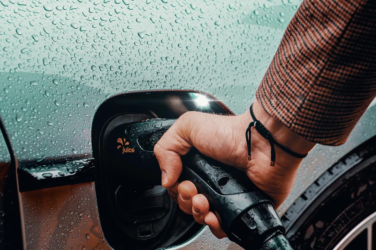 A hand plugging a charging connector into an electric car in the rain