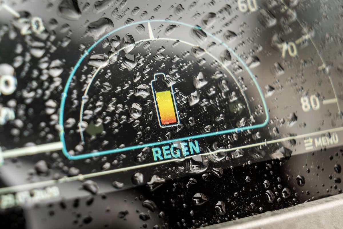 An EV dashboard battery gauge seen through raindrops on the windscreen